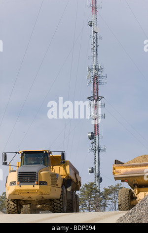 Scavatrice in un cantiere con una torre cellulare in background Foto Stock