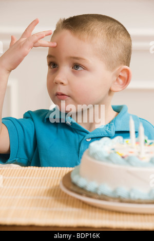 Ragazzo firma la parola 'Sick' in American Sign Language seduto davanti a una torta di compleanno Foto Stock