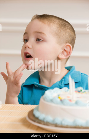 Ragazzo firma la parola 'Compleanno' in American Sign Language seduto davanti a una torta di compleanno Foto Stock