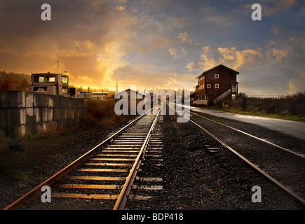 Un binario ferroviario che conduce a distanza attraverso una piccola stazione al tramonto Foto Stock