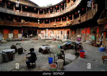 Cestello cinese weaver seduti nel cortile di una casa rotonda, cinese: Tulou, adobe casa rotonda della minoranza Hakka, Tianl Foto Stock