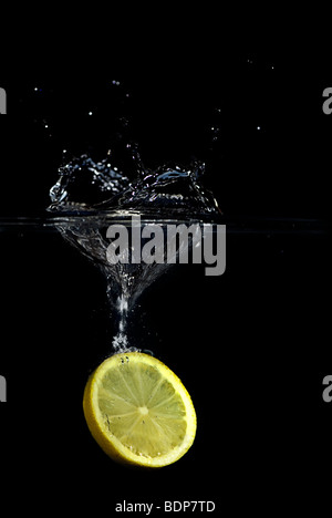 Un limone è caduto nell'acqua creando una splash e bolle. Isolato su nero. Foto Stock