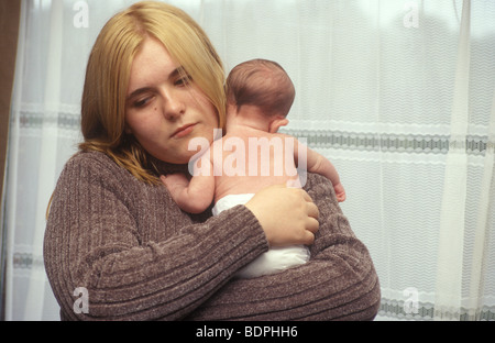 La mamma adolescente cercando tenendo premuto il suo bambino Foto Stock