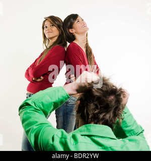 Studio shot foto su sfondo isolato di due sorelle twin donne amici di fronte ad un uomo lo strappo i suoi capelli lontano Foto Stock