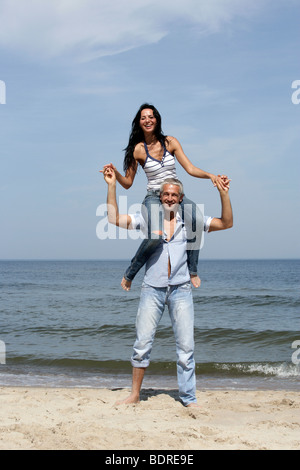 Donna attraente a cavallo di uomo di spalle sulla spiaggia Foto Stock