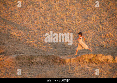 Giovane ragazza birmano in esecuzione attraverso un risone campo nei pressi di Mrauk U, Divisione di Rakhine, Arakhan unito, MYANMAR Birmania, a sud-est Foto Stock