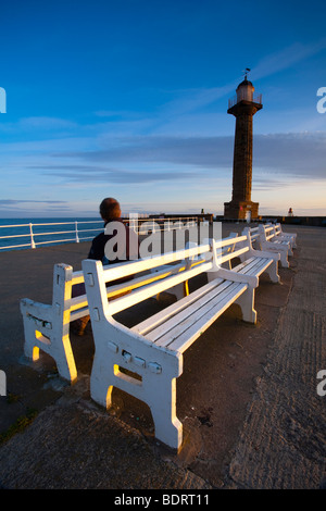 Inghilterra, North Yorkshire, Whitby. Persona seduta su una panchina sul molo a Whitby. Foto Stock