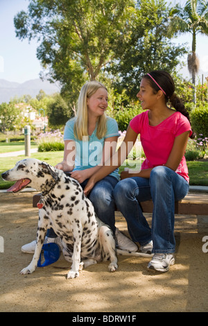 Ispanico e Caucasico junior Tween tween ragazze seduto e parlando nel parco. Signor diverseTween tweens proprietario del cane vista frontale © Myrleen Pearson Foto Stock