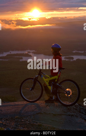 Femmina ciclista in discesa al sole di mezzanotte, Lapponia, Svezia Foto Stock