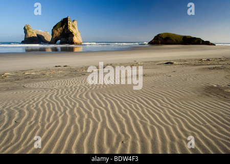 Le dune di sabbia e da potenti surf roccia scolpita isole con grotte e archi a Wharariki Beach, Nuova Zelanda Foto Stock