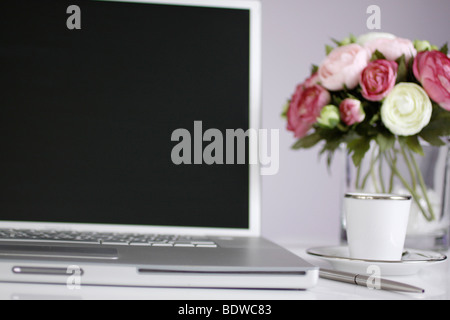 Argento portatile su una scrivania con una tazza di caffè espresso, una penna e un vaso con graziosi fiori rosa e bianchi accanto ad essa. Foto Stock