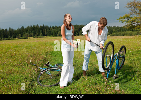Coppia giovane di prato soleggiato, giovane uomo che ripara un vecchio stile bike Foto Stock