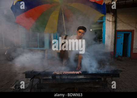 KASHGAR, Cina ,Uyghur uomo spiedini di cottura in corrispondenza di un bordo strada stallo in una nuvola di fumo. Foto Stock