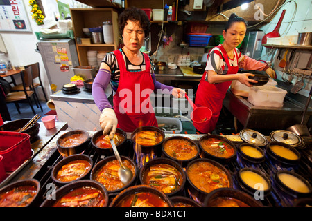 Donna di cottura jiggae piccante o stufato nel mercato Namdemun in Seoul COREA DEL SUD Foto Stock