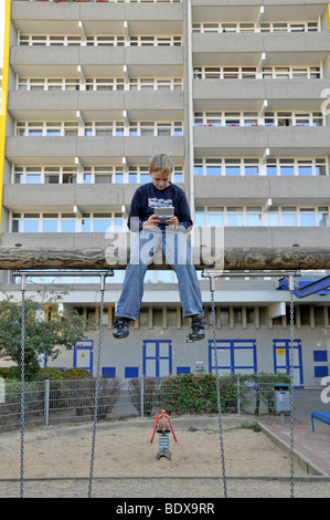 Ragazzo, 9, giocando con il suo Nintendo nella parte anteriore di un alto edificio di appartamenti, città satellite di Chorweiler a Colonia, Nord Rh Foto Stock