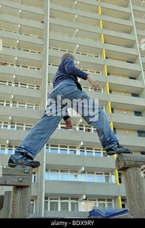 Ragazzo, 9, giocando su un parco giochi a fronte di un alto edificio di appartamenti, città satellite di Chorweiler a Colonia, Nord Rhin Foto Stock