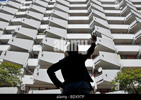 Ragazzo in piedi di fronte ad un alto edificio di appartamenti con balconi e parabole satellitari, città satellite di Chorweiler in Co Foto Stock