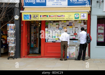 Due uomini guardando gli annunci pubblicitari in una edicola Negozio finestra, London, England, Regno Unito Foto Stock