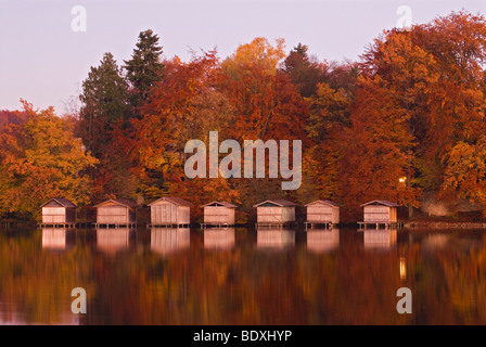 Boathouses e i loro riflessi nelle calme acque del lago Wesslinger vedere circondato da fogliame autunnale Wessling, Baviera, Ger Foto Stock