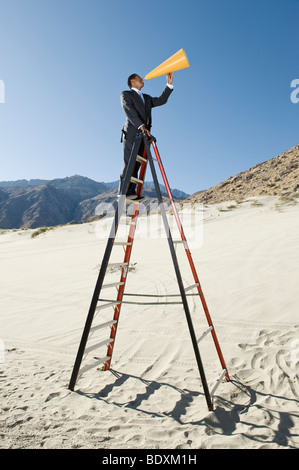 Imprenditore su scala utilizzando megafono nel deserto Foto Stock