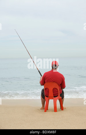 Uomo in rosso tshirt pesca dal rosso sedia in plastica, Cape Town, Sud Africa Foto Stock