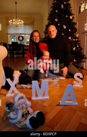 Famiglia con bambino nella loro addobbate a festa soggiorno a Natale Foto Stock