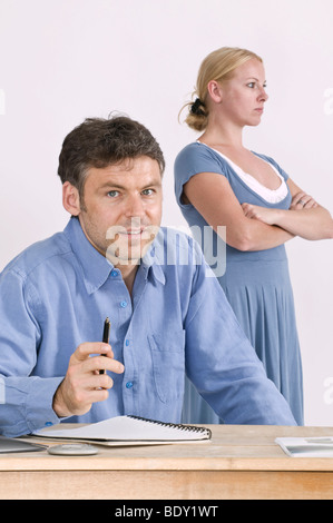 Colleghi di lavoro in un ufficio, donna che guarda indifferente, dietro l'uomo Foto Stock