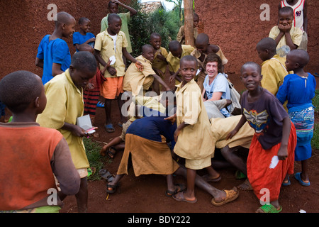 Un bianco pubblico scolaro viene assaliti da bambini africani in un villaggio ruandese durante una visita della scuola. Foto Stock