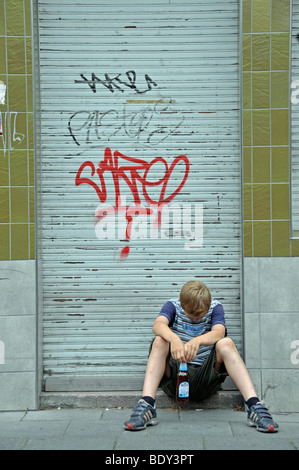 Lonely nove-anno-vecchio ragazzo davanti ad un negozio chiuso cosparse di graffiti, Germania, Europa Foto Stock