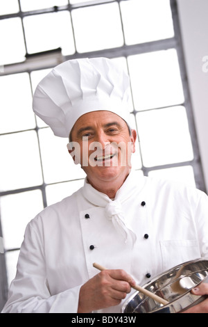 Lo Chef indossando un chef hat agitazione in una pentola Foto Stock