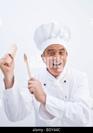 Lo Chef indossando un chef hat tenendo un cucchiaio di legno e un matterello nelle sue mani Foto Stock