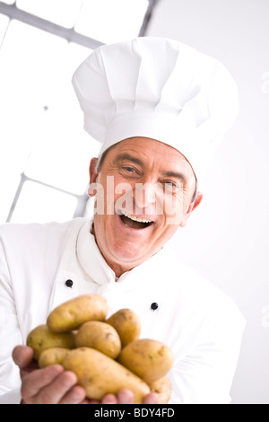 Lo Chef indossando un chef hat holding di patate nella sua mano Foto Stock