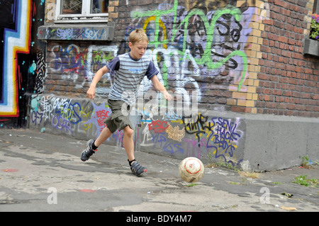 Nove-anno-vecchio ragazzo giocando con il suo calcio di fronte a un muro di graffiti, area kickabout a Colonia, nella Renania settentrionale-Vestfalia, Ger Foto Stock