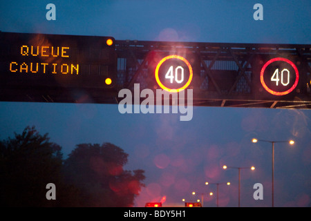 Velocità ridotta luci sul tettuccio di gantry su autostrada per informare i conducenti di accodamento di traffico, Inghilterra. Foto Stock