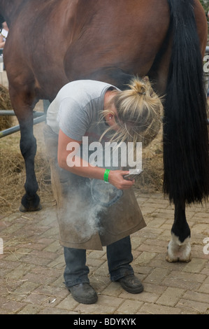 Una femmina di apprendista maniscalco montaggio di un ferro di cavallo per cavalli zoccolo in un paese mostrano in Essex. Foto Stock