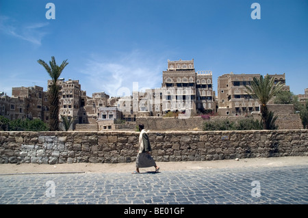 Un uomo passeggiando passato case a torre in una zona pedonale della città vecchia di Sana'a, Yemen. Foto Stock