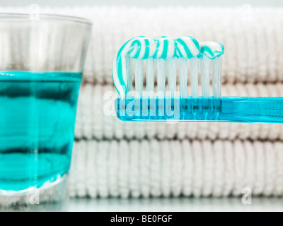 Un blu spazzolino da denti con dentifricio, un bicchiere pieno di un colluttorio e asciugamani sullo sfondo. Foto Stock