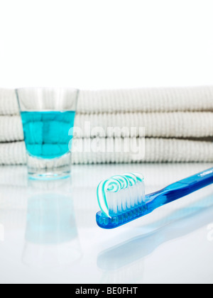 Un blu spazzolino da denti con dentifricio, un bicchiere pieno di un colluttorio e asciugamani sullo sfondo. Foto Stock