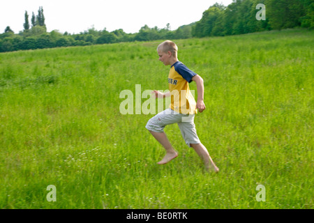 Ragazzo giovane correre a piedi nudi attraverso un prato Foto Stock