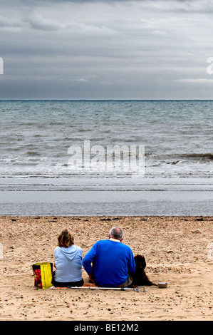 Un giovane seduto sulla spiaggia in una fredda giornata di Camber Sands in East Sussex. Foto Stock