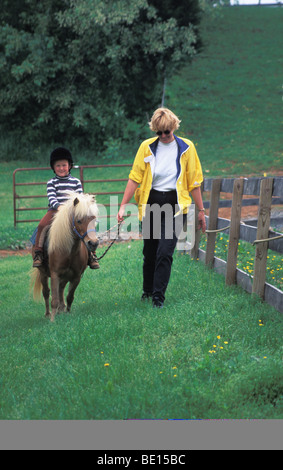 Un bambino cavalca un pony su una farm di Virginia sotto sua madre guida.(modello rilasciato) Foto Stock