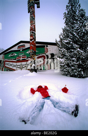 Longhouse e Totem Pole in Thunderbird Park, Victoria, BC, Isola di Vancouver, British Columbia, Canada - donna fare Angelo di Neve Foto Stock