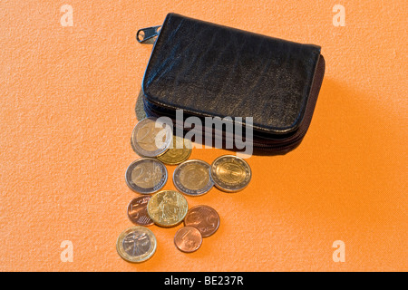 Aperto a metà nero borsa in pelle con cambio allentata disteso su un supporto di colore arancione. Porte-monnaie noir et menue monnaie. Foto Stock