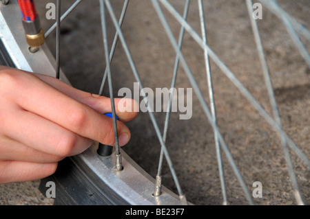 Un ragazzo le viti sul coperchio di una valvola per bicicletta dopo il pompaggio fino al pneumatico. Foto Stock