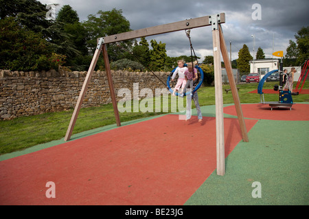 Bambini che giocano su swing protetti da sicurezza attività di gomma materassino a Broadway Activity Park WORCESTERSHIRE REGNO UNITO Foto Stock