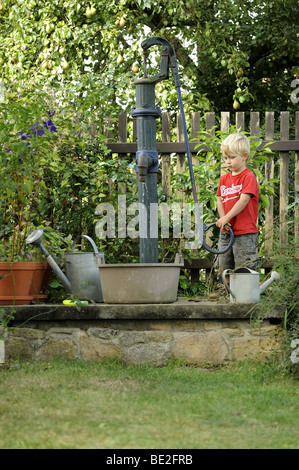 Un bambino di tre anni ragazzo gioca con un esterno di vintage a mano la pompa acqua giardino Foto Stock