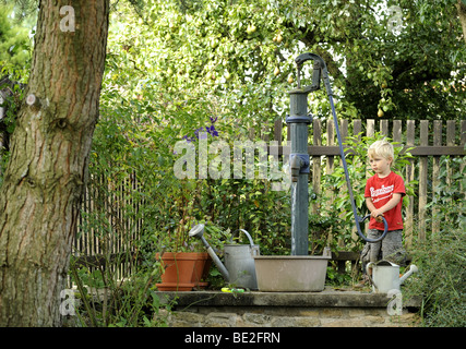Un bambino di tre anni ragazzo gioca con un esterno di vintage a mano la pompa acqua giardino Foto Stock