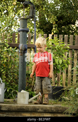 Un bambino di tre anni ragazzo gioca con un esterno di vintage a mano la pompa acqua giardino Foto Stock