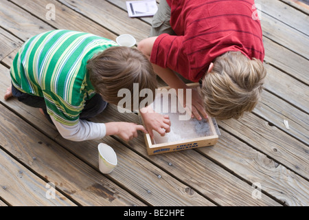 Due ragazzi sbirciare baby garter snake in una scatola, all'aperto Foto Stock