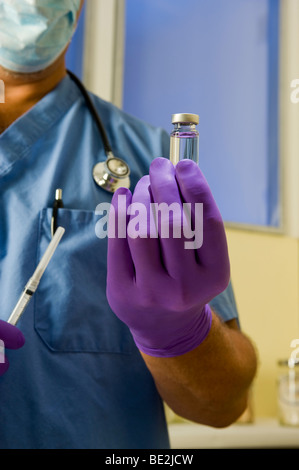 Maschio di medico o infermiere indossando blue scrubs, uno stetoscopio e guanti mantiene la fiala di sostanza farmaceutica e la siringa. Foto Stock